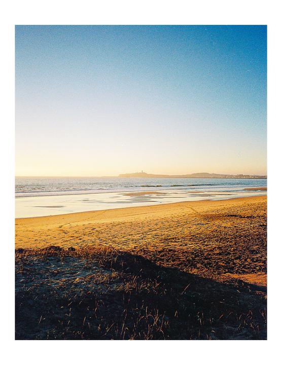 A sandy beach with gentle waves under a clear sky during golden hour.