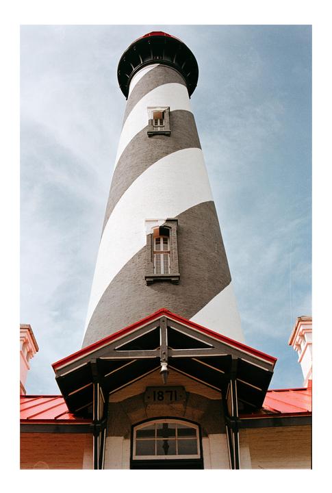 A tall lighthouse with black and white stripes stands against a blue sky.