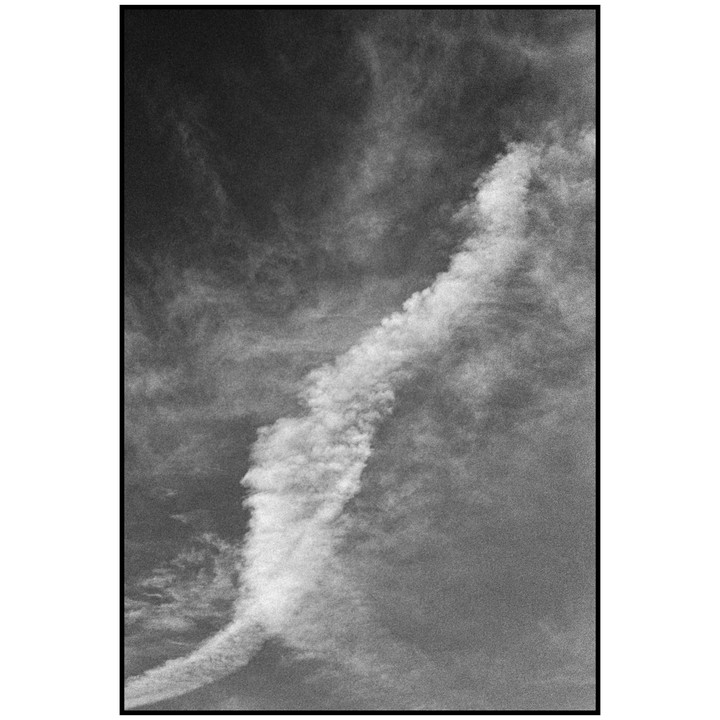 A thick contrail curves across a cloudy sky.