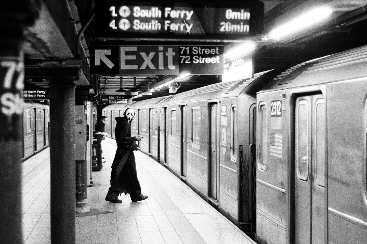 A person in a Scream mask and robe stands on a subway platform next to a train.