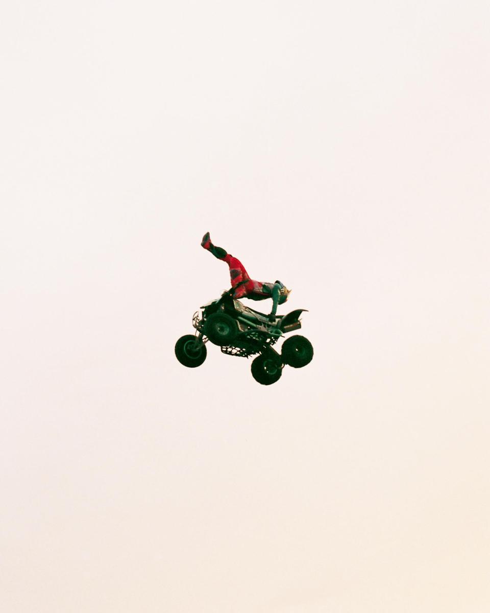A person in red and green clothing is performing a stunt on an ATV in mid-air against a light background.