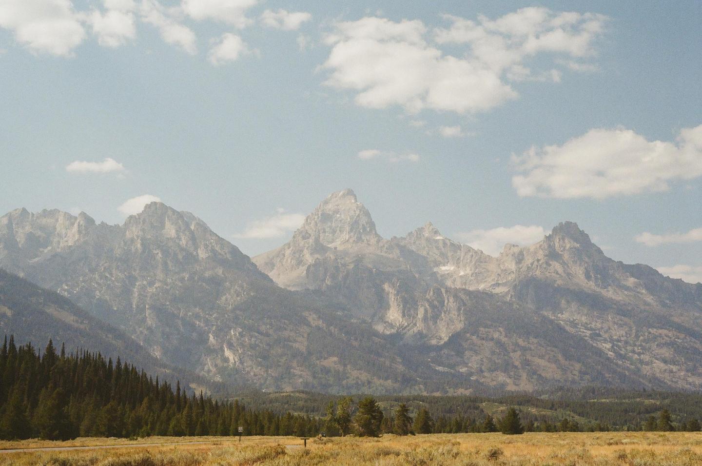A mountain range with a forest in the foreground is visible under a hazy sky with scattered clouds.