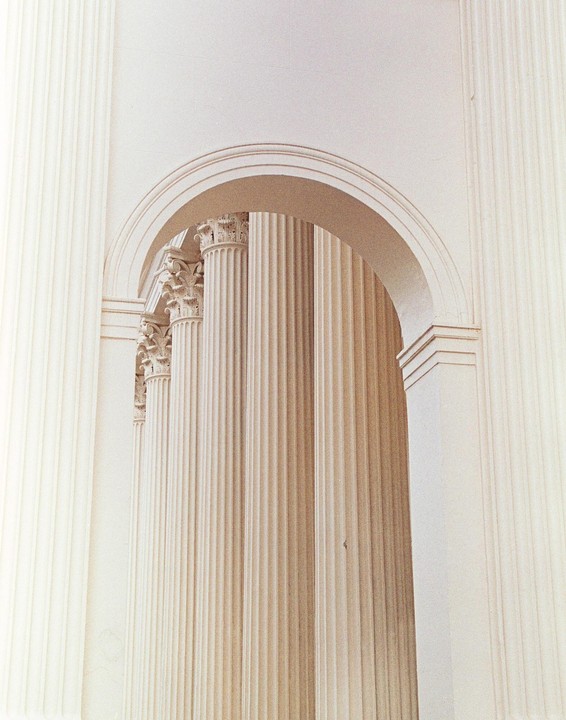 An archway frames a series of fluted columns, some with ornate capitals.