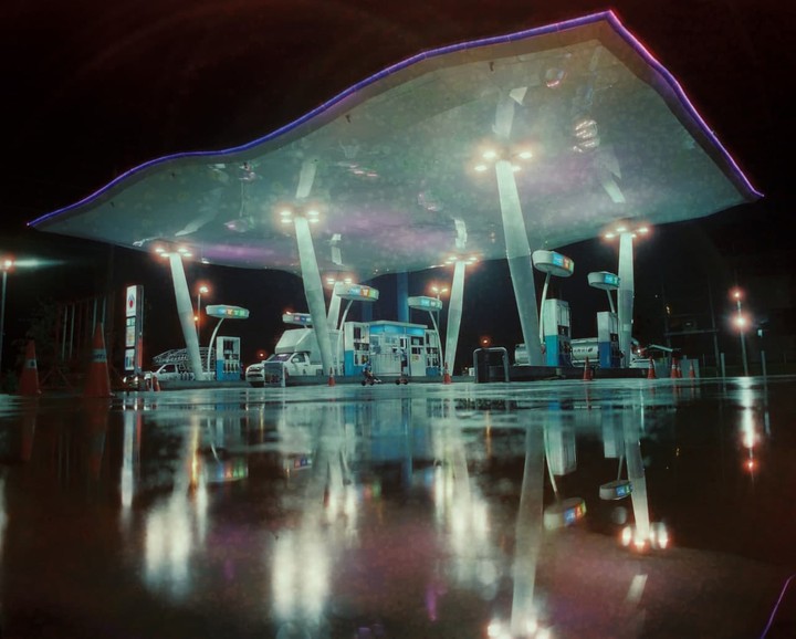 A gas station with a large, illuminated canopy is reflected in a wet ground at night.