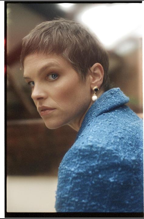 A woman with short hair and a blue jacket looks over her shoulder.