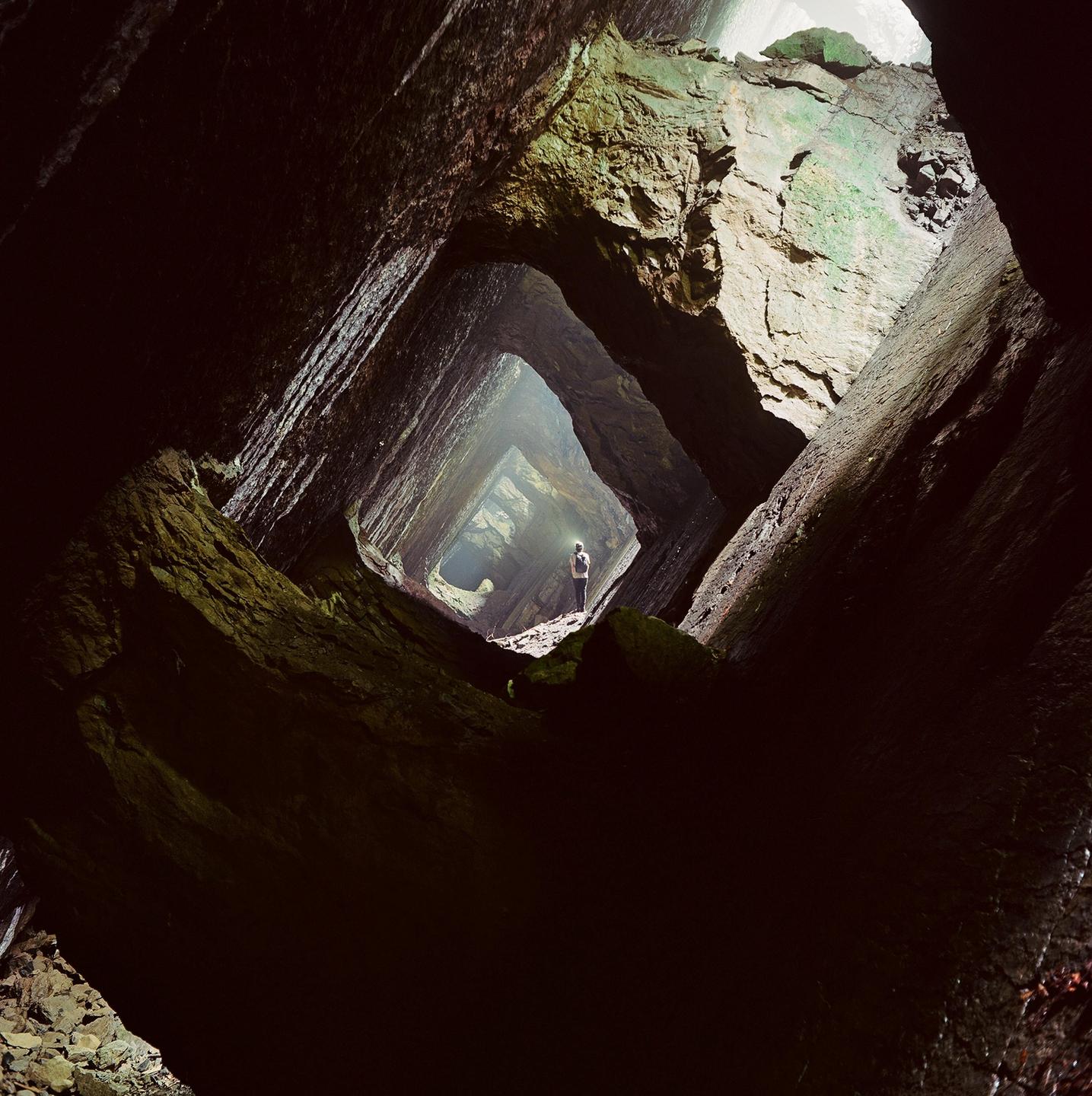 A person stands in a dark mine tunnel with light visible at the end.