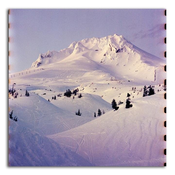 A snow-covered mountain with ski tracks and evergreen trees is visible under a clear sky.