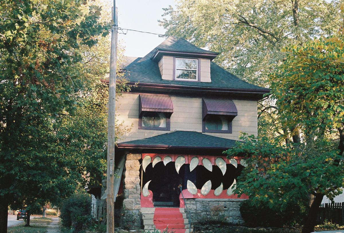 A house decorated to look like a monster with large teeth is surrounded by trees.