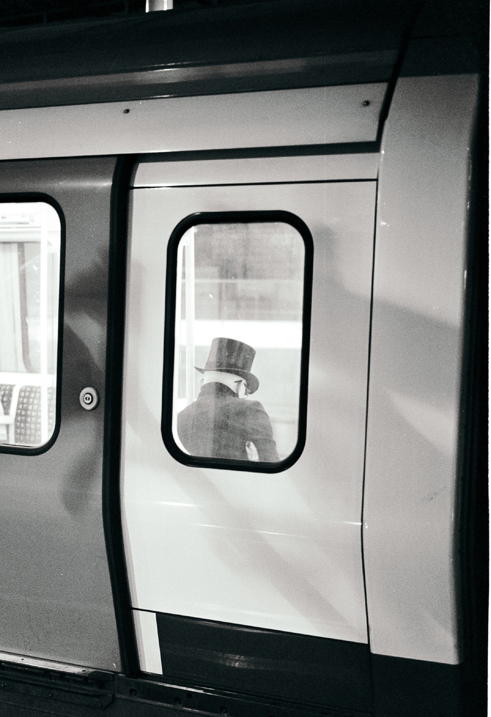 A man wearing a top hat is visible through the window of a train door.