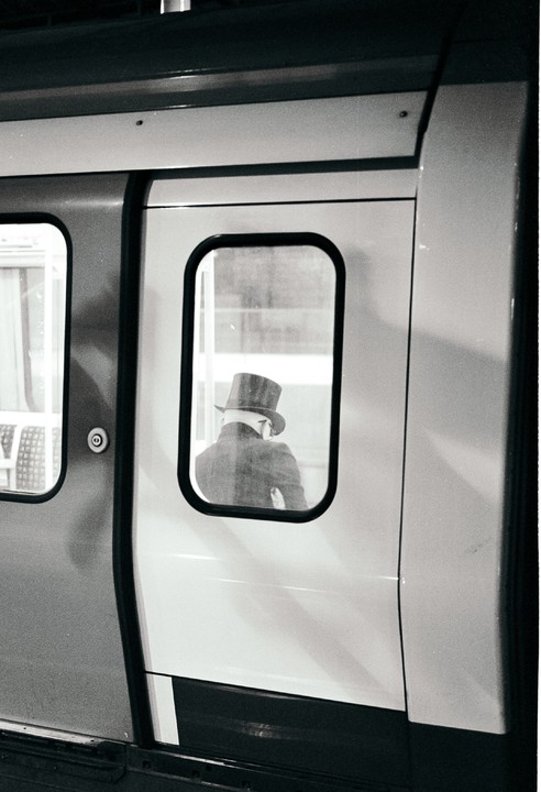 A man wearing a top hat is visible through the window of a train door.