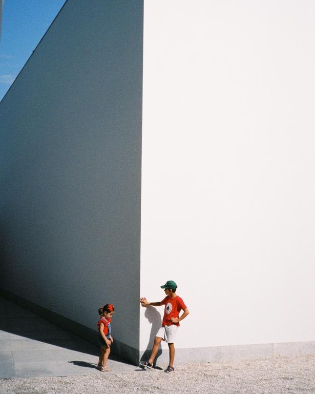 A boy and a girl stand next to a large white wall with a shadow cast on it.