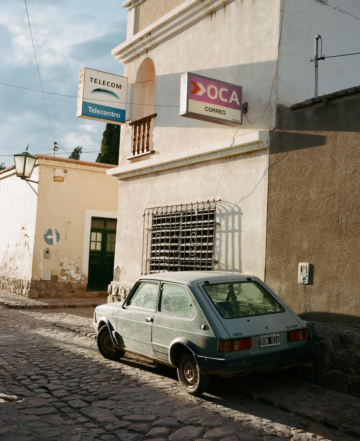 A small car is parked on a cobblestone street next to a building with signs for Telecom and Oca.