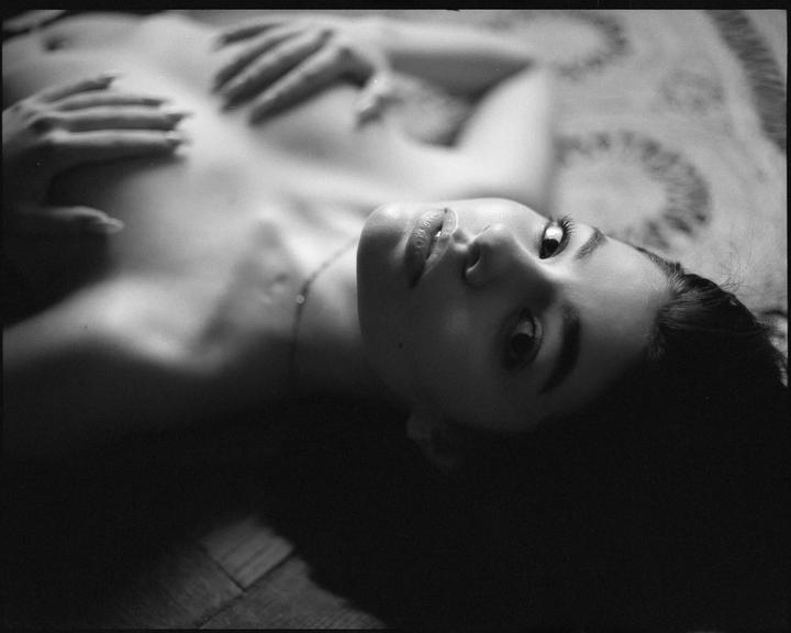 A woman lies on her back with her hands on her chest, looking up at the viewer.