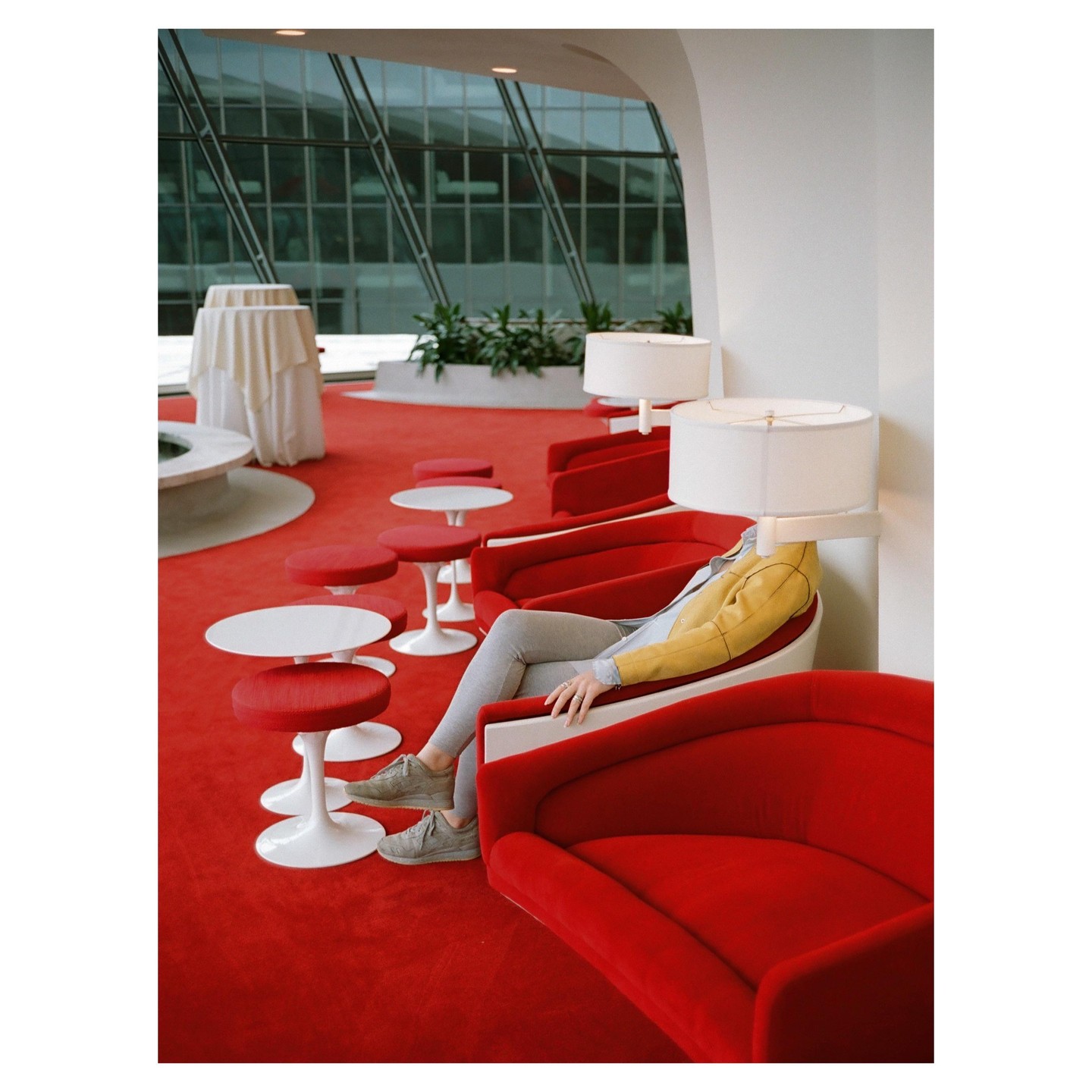 A person sits in a red chair with a lamp in front of their head, surrounded by red carpet and furniture.