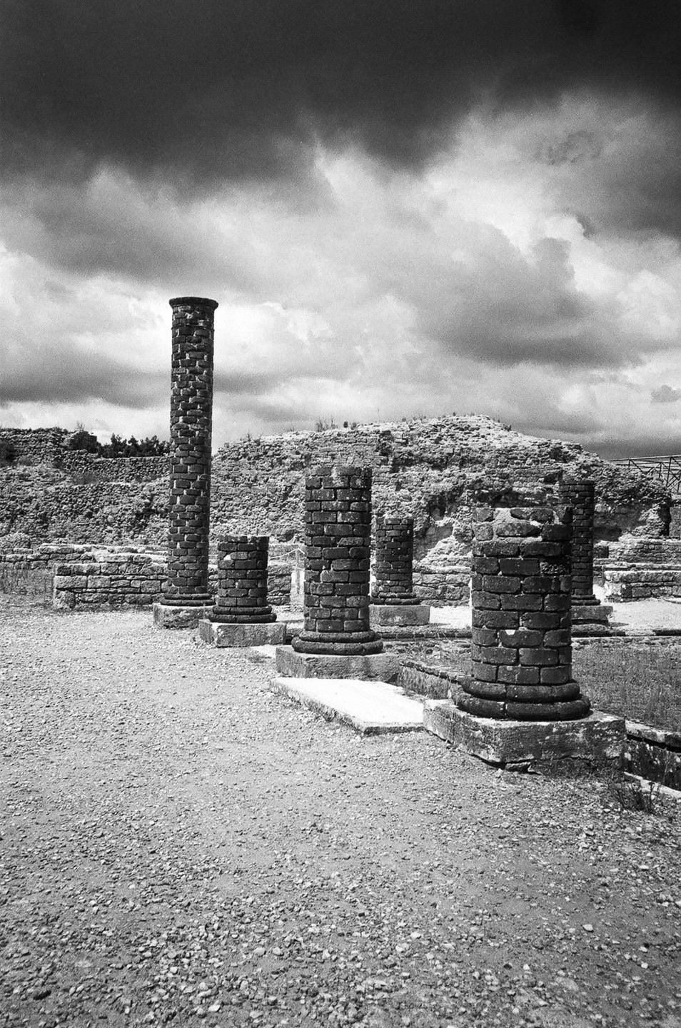 Several ancient stone columns stand among ruins under a dramatic cloudy sky.