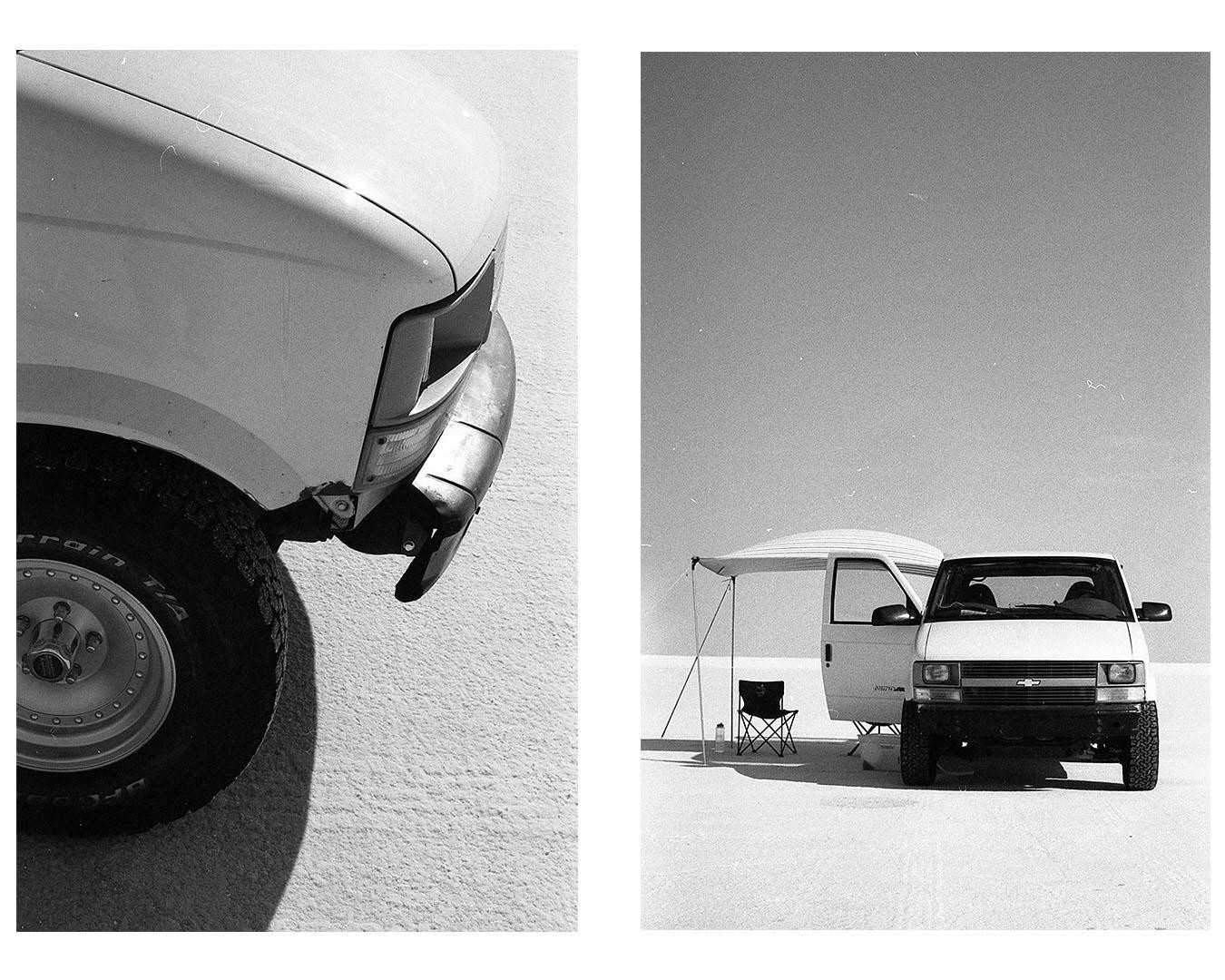 A white van with an open door and an awning is parked on a salt flat under a clear sky.