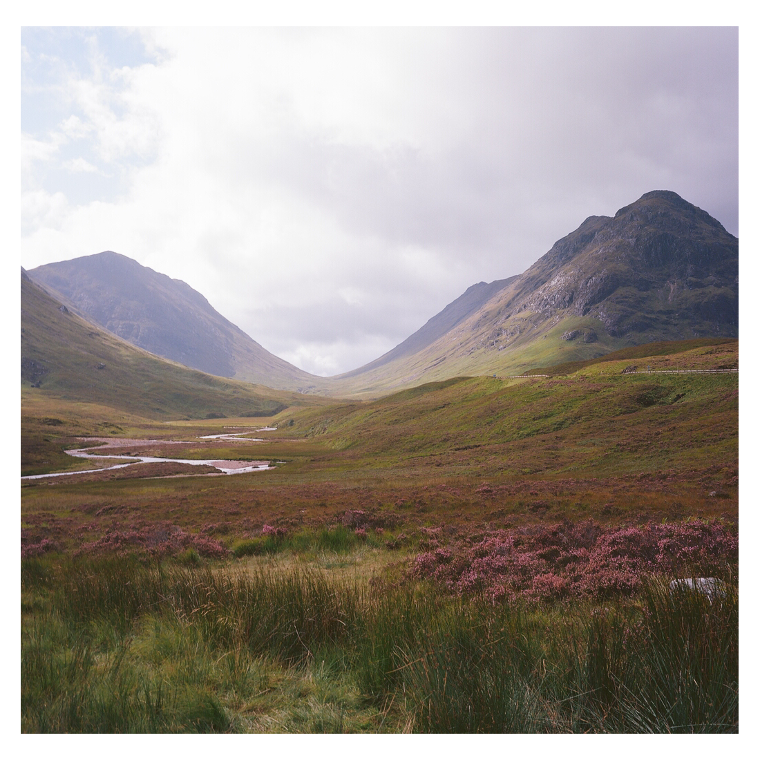 A winding river flows through a valley with mountains on either side under a cloudy sky.