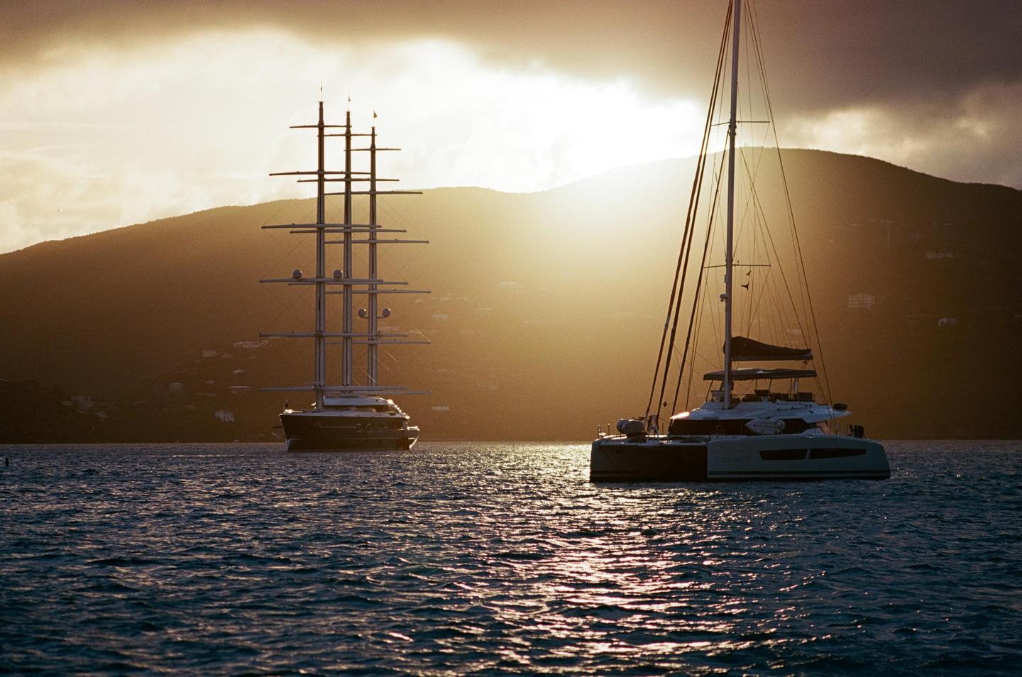 Two boats are on the water with a mountain and a bright sky in the background.
