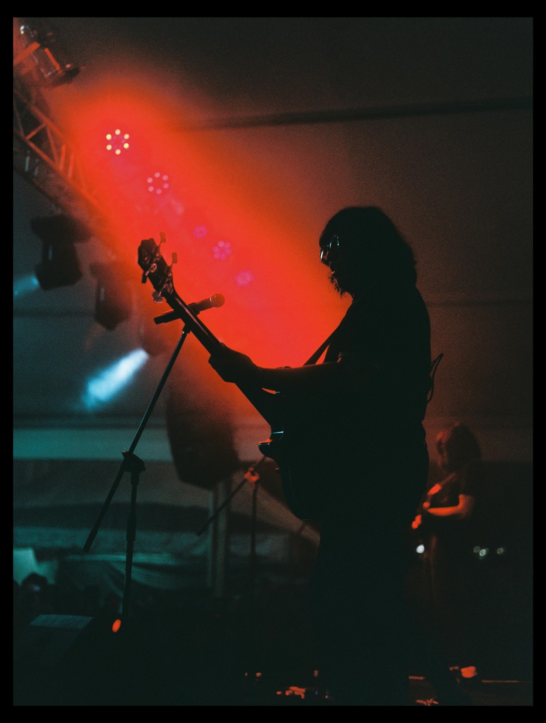 A musician is playing a guitar on a stage with red and blue lights.