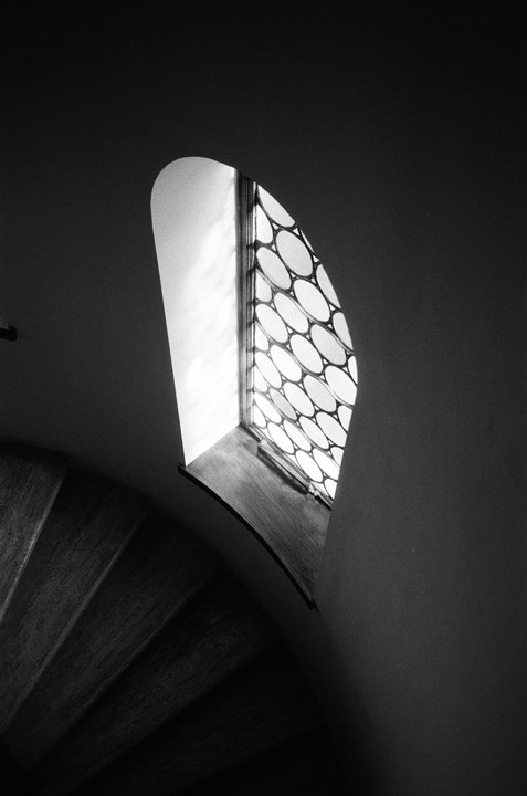 A spiral staircase descends from a window with a circular pattern.