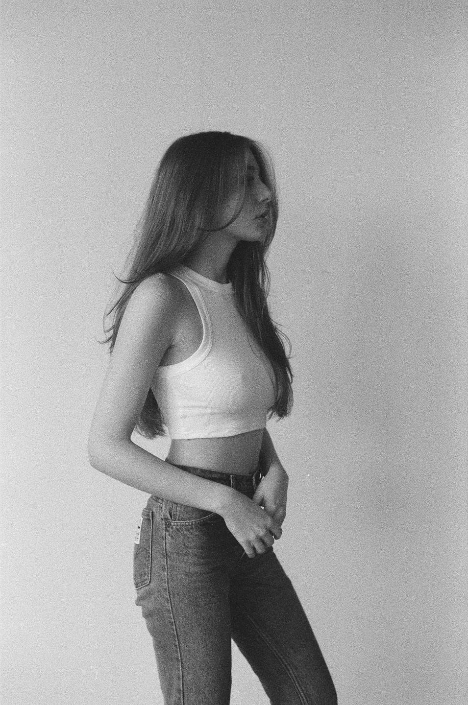 A woman with long hair stands in profile, wearing a crop top and jeans.