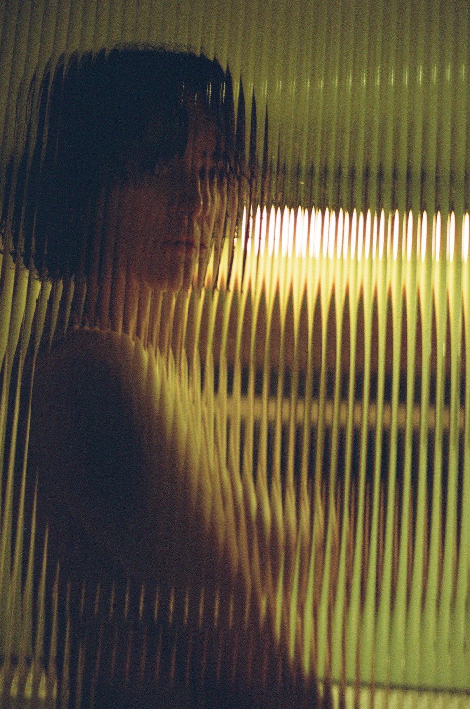 A woman is visible through a textured glass panel with a bright light source behind her.