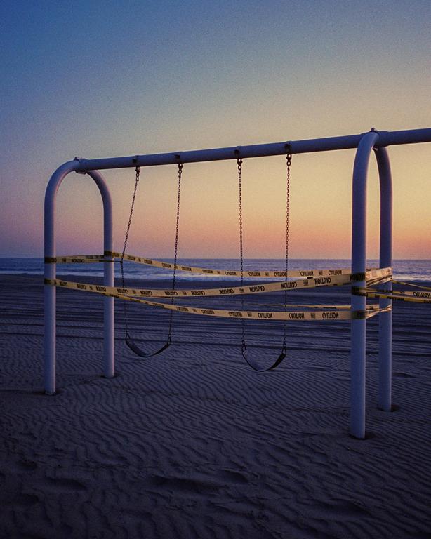 A swing set on a sandy beach is wrapped with caution tape at sunset.