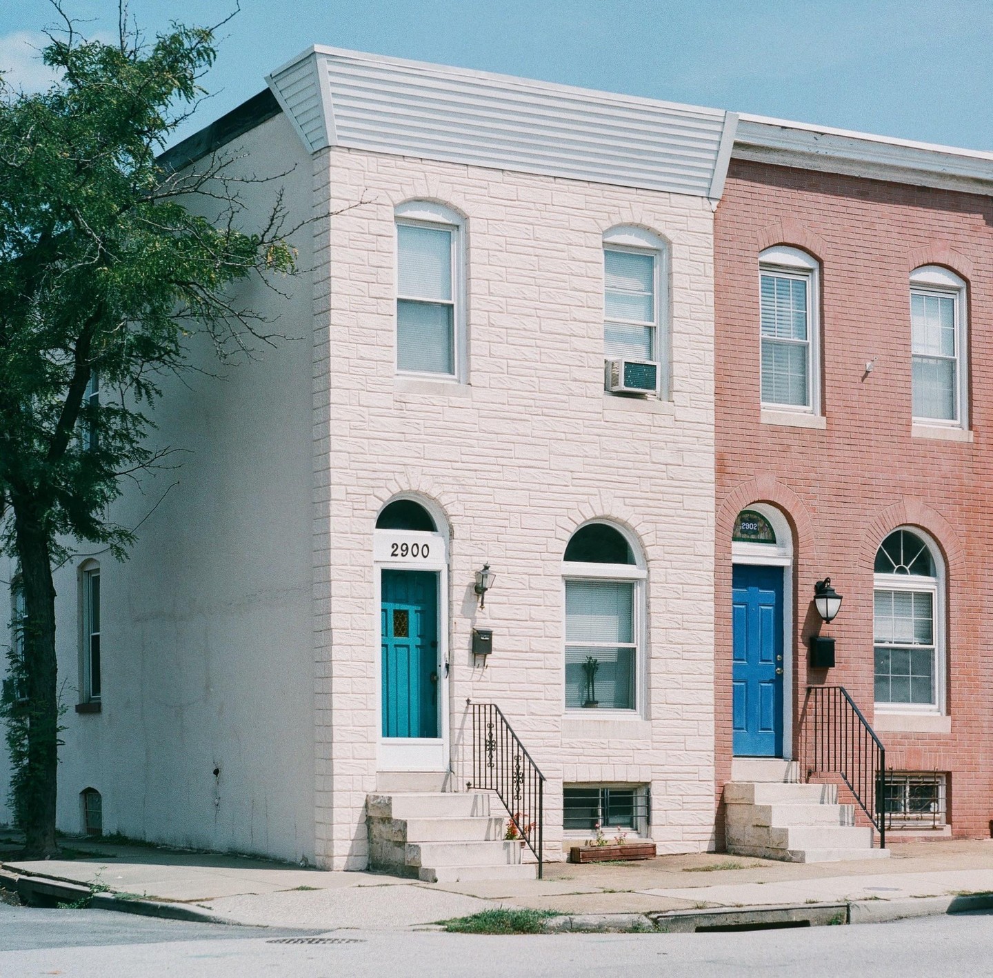 Two row houses with blue doors and white steps are visible from a street corner.