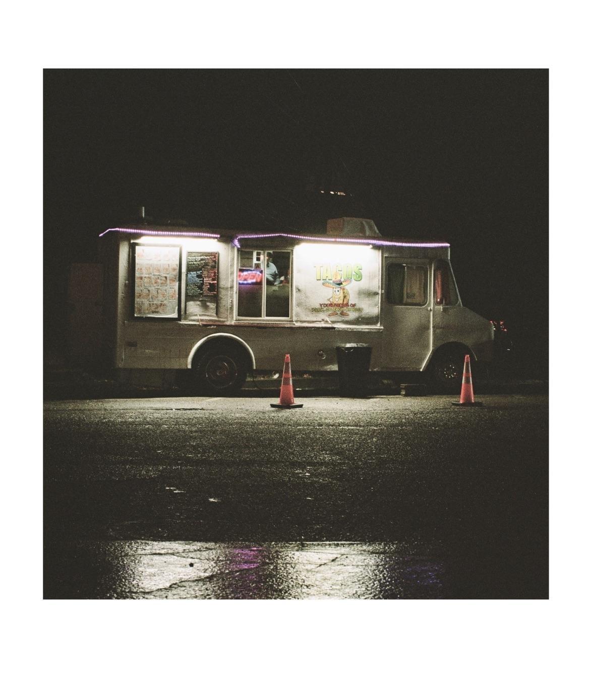 A food truck with glowing lights is parked on a wet street at night.