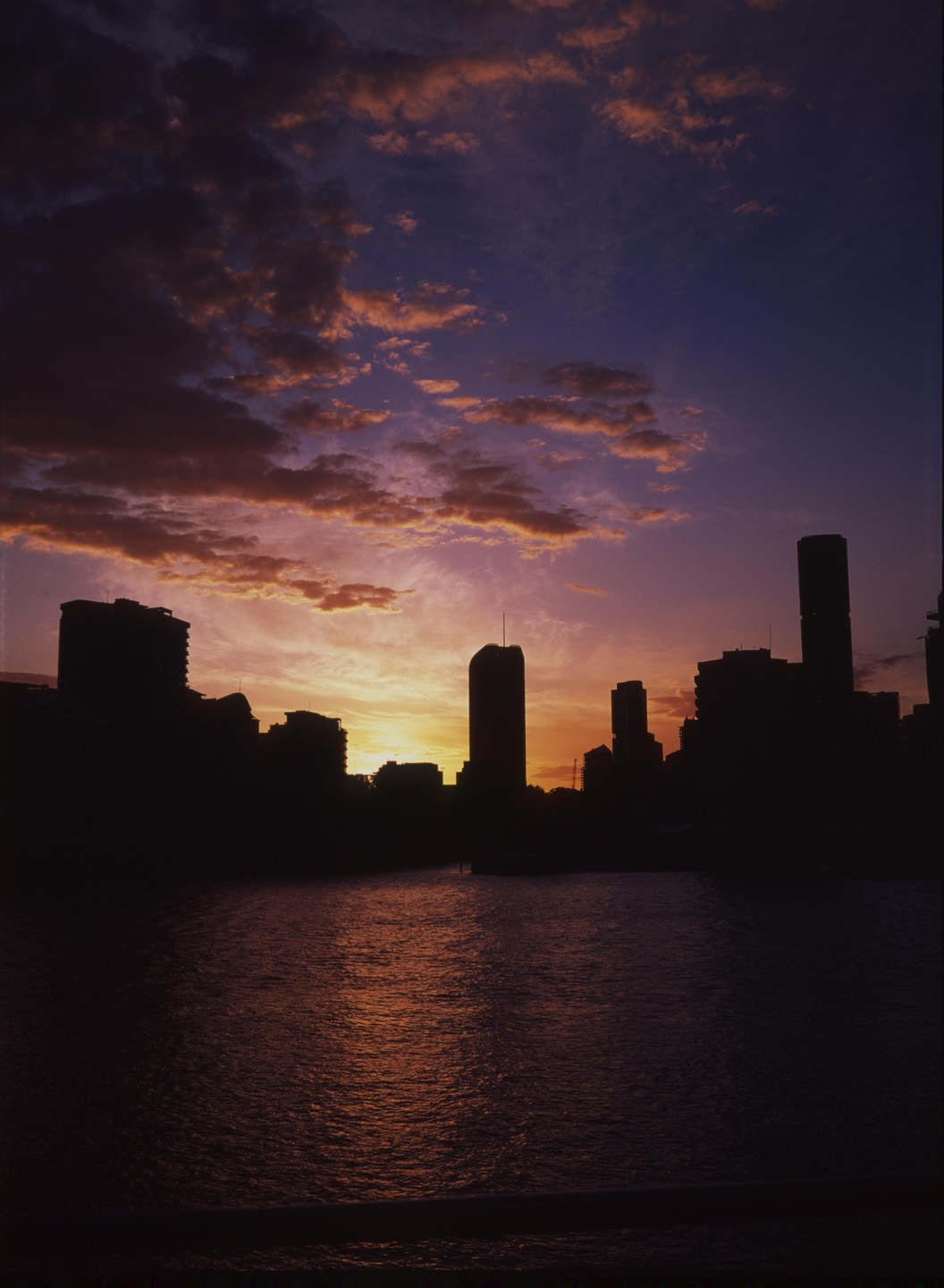 A city skyline is silhouetted against a vibrant sunset over a body of water.