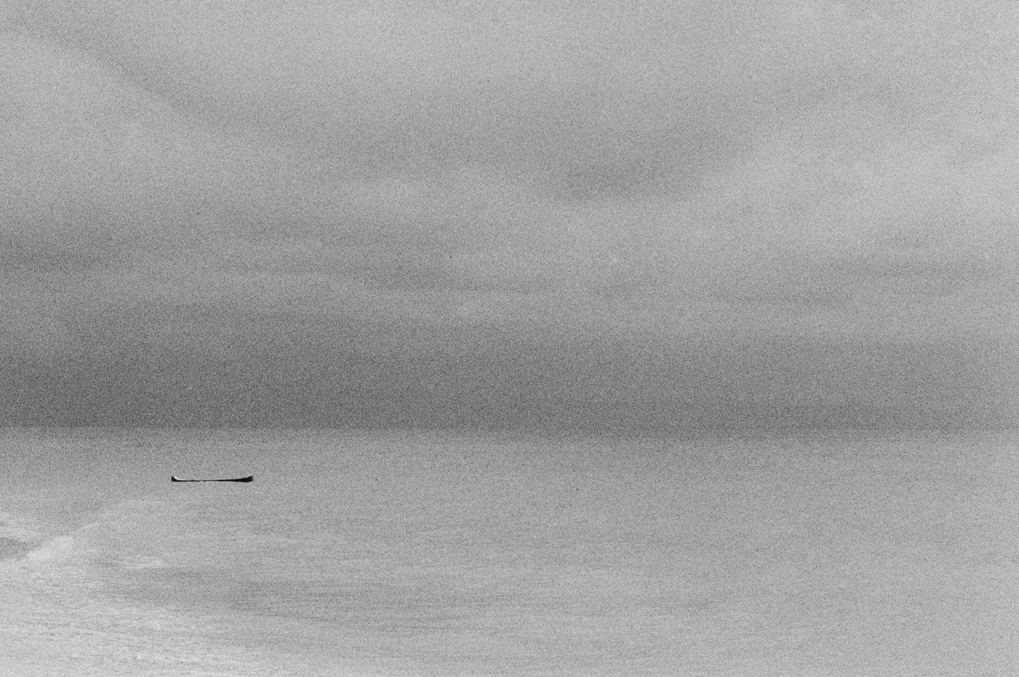 A small boat floats on a calm body of water under a hazy sky.