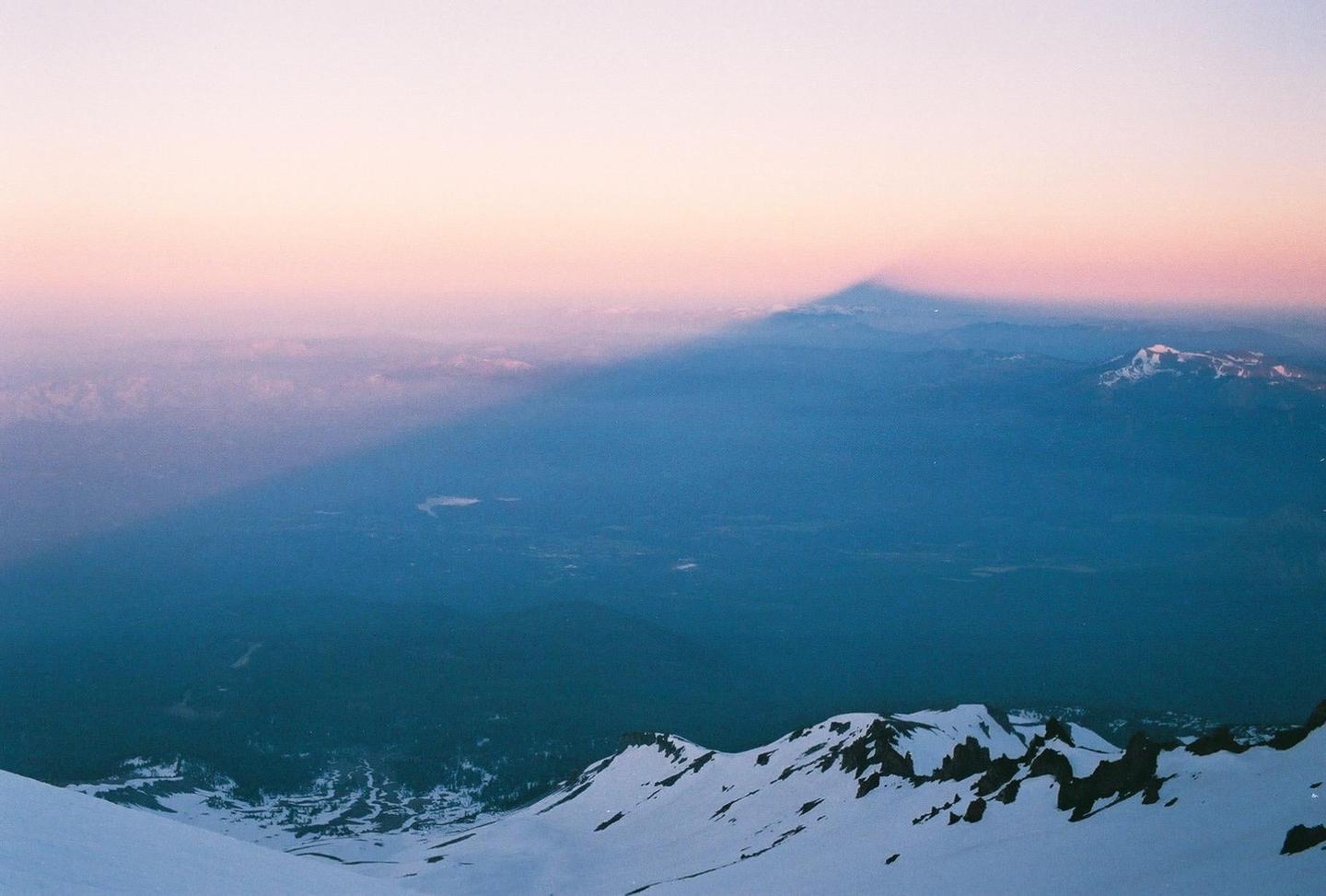 A mountain casts a long shadow over a valley at sunrise.