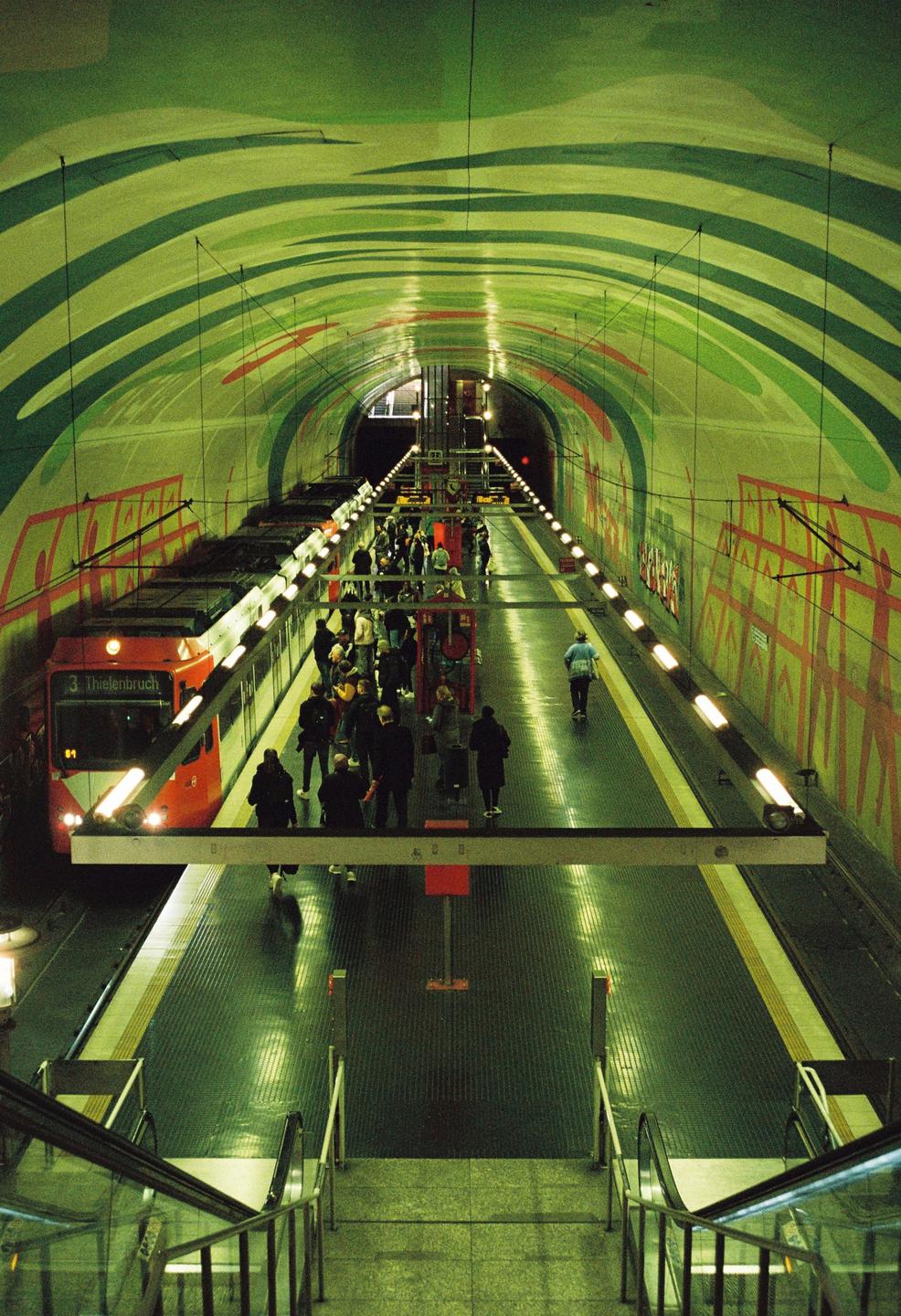 A red train is stopped at a subway station with a green and red painted tunnel.