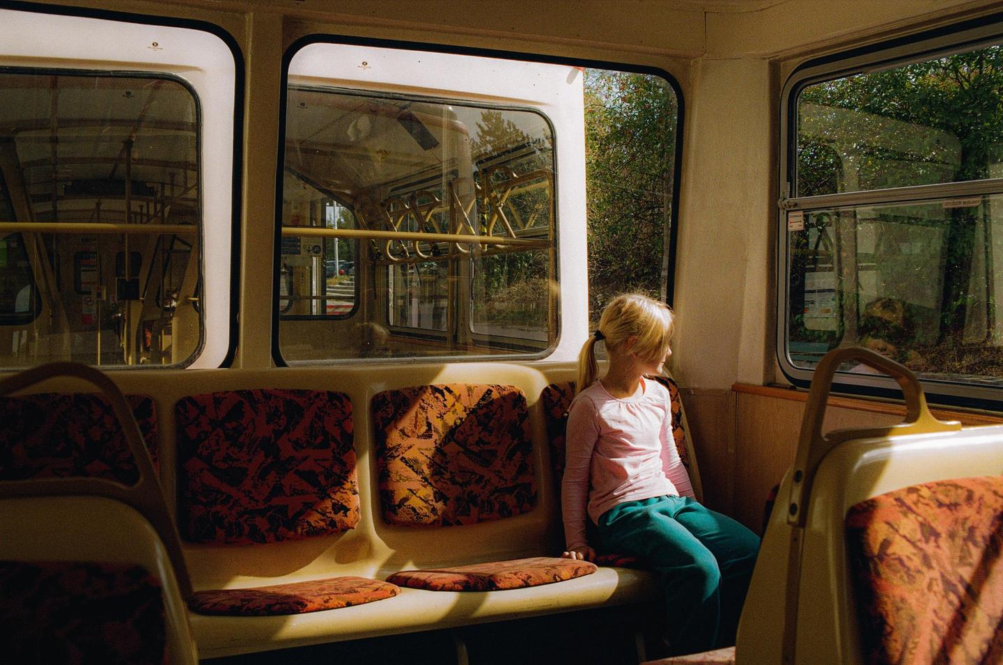 A girl with a ponytail sits on a bus seat looking out the window.