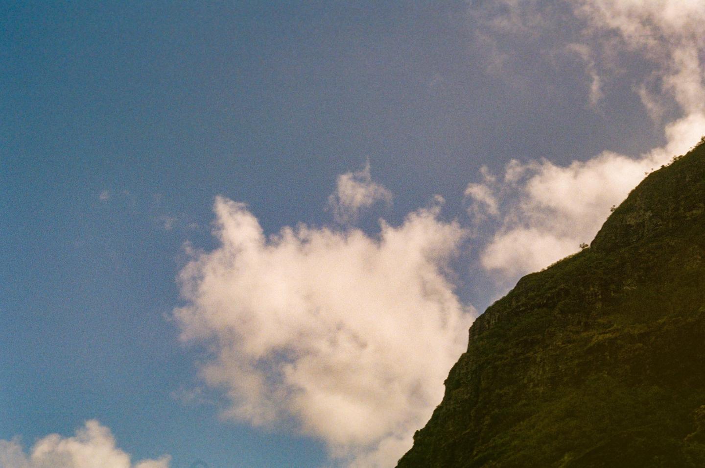 A large, green mountain slope is visible on the right side of the frame, with a blue sky and white clouds filling the rest of the image.