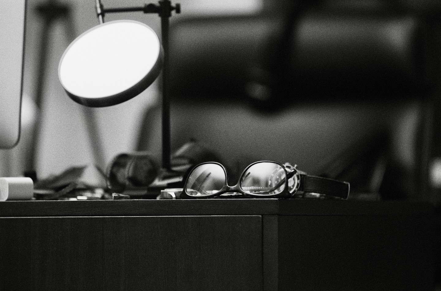 A pair of eyeglasses rests on a dark surface next to a lamp and other items.