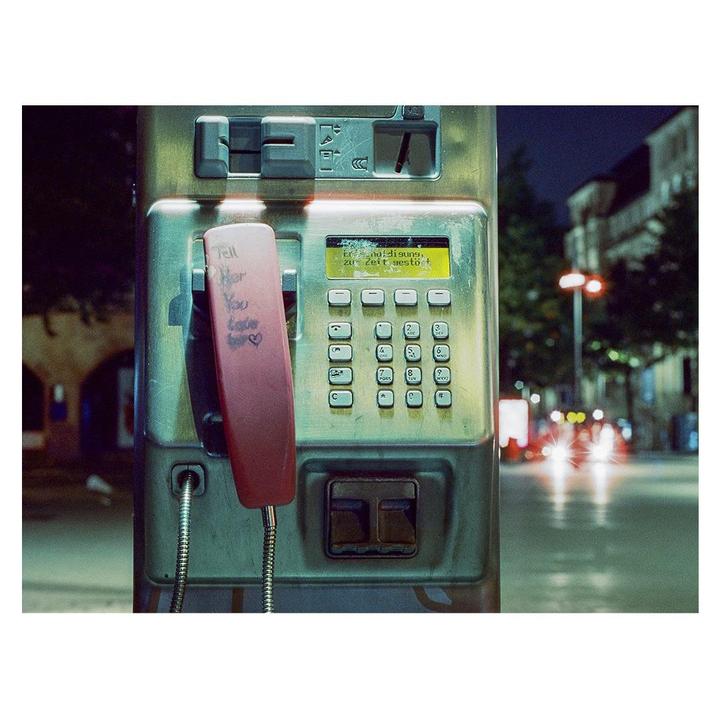 A payphone with a red receiver and a note that says "Tell her you love her" is shown at night.