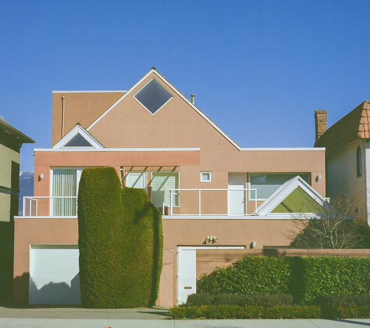 A modern house with a peach-colored facade and a large green hedge in front of it stands under a clear blue sky.