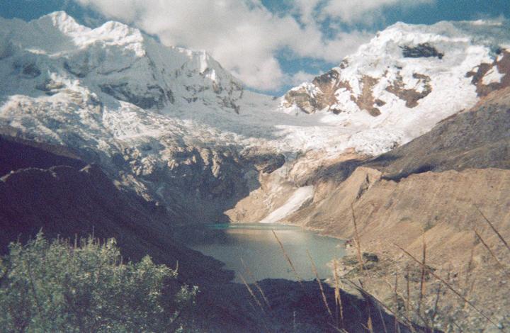 A glacial lake is nestled between snow-capped mountains under a cloudy sky.