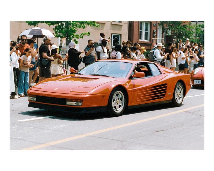 A red sports car drives down a street lined with people watching.