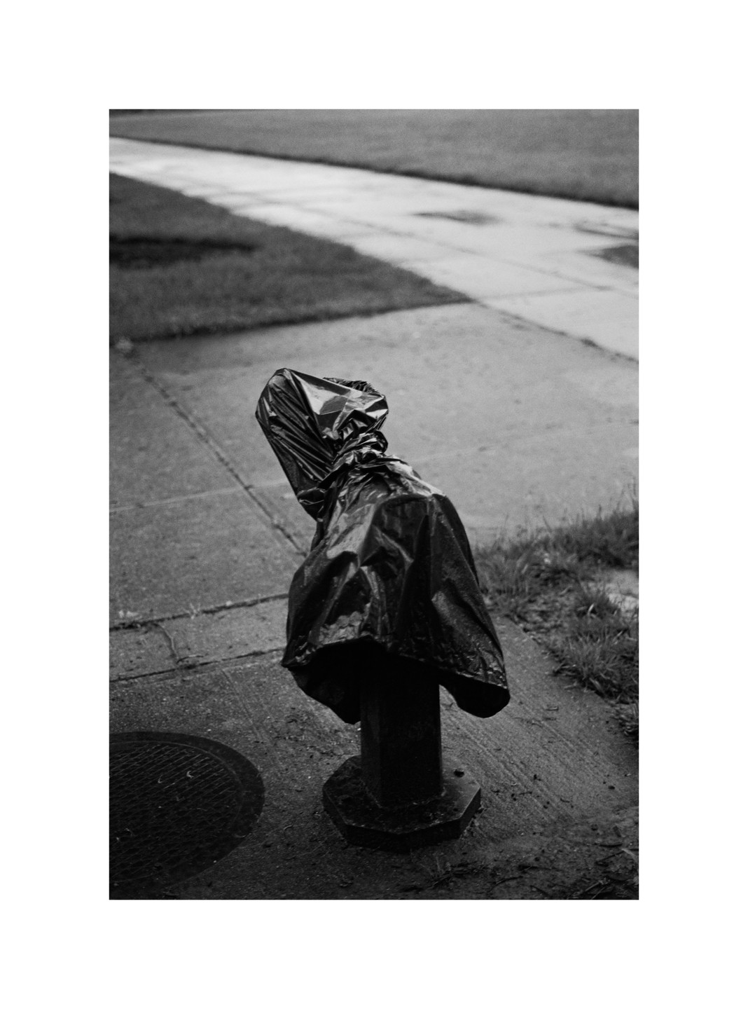 A water fountain covered with a black plastic bag stands on a sidewalk next to a grassy area.