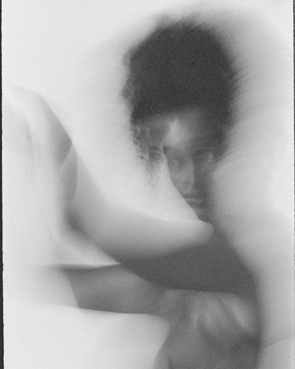 A man with dark, curly hair is visible through a soft, blurry, and high-contrast filter.