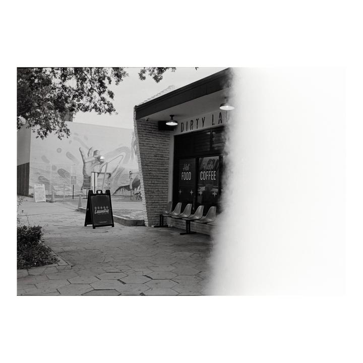 A black and white street view shows a laundry and coffee shop with a mural on the adjacent building.