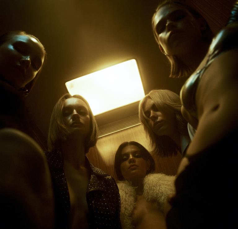 Five women are looking down at the camera in an elevator.
