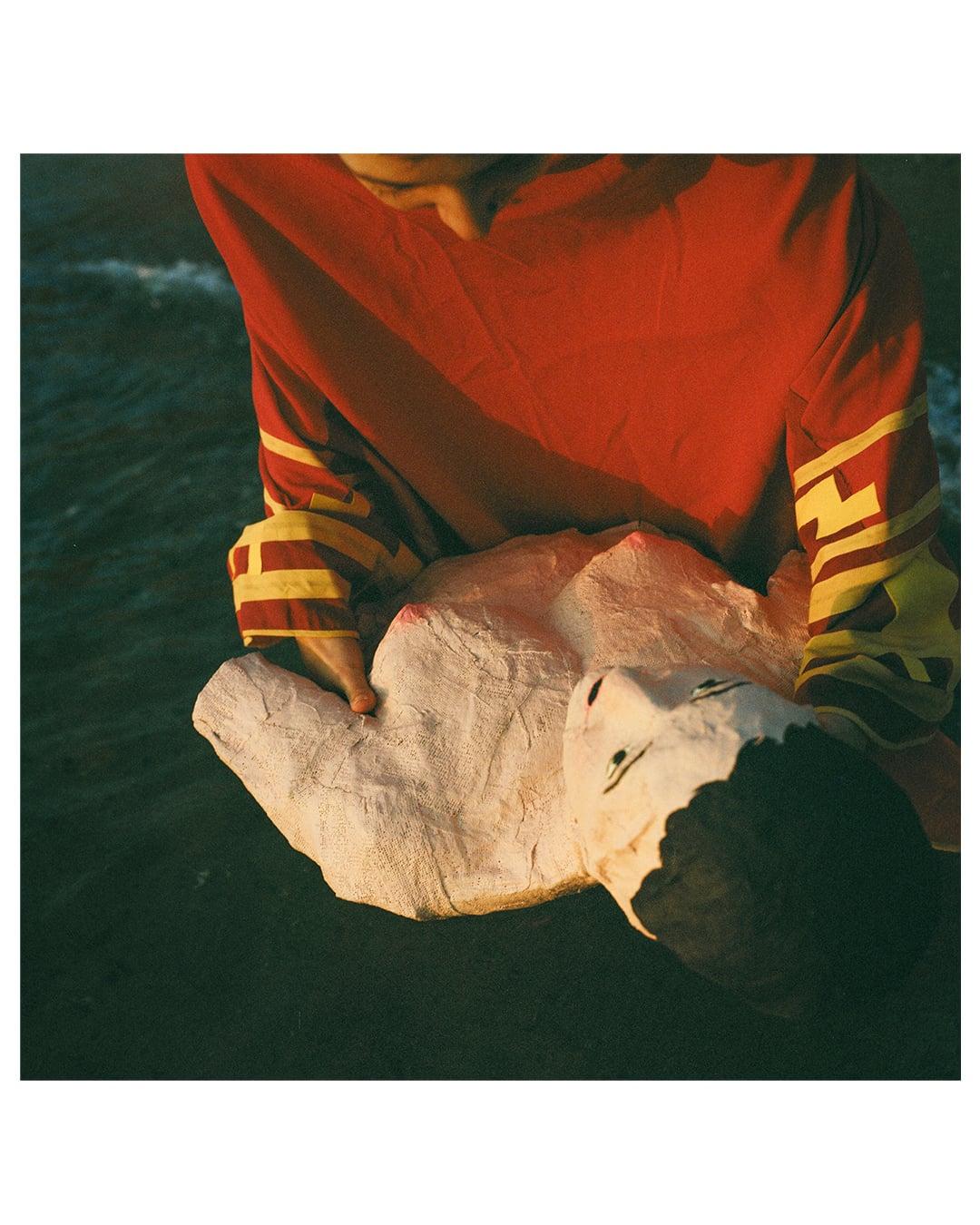 A person in a red shirt holds a white sculpture of a torso and head over dark water.