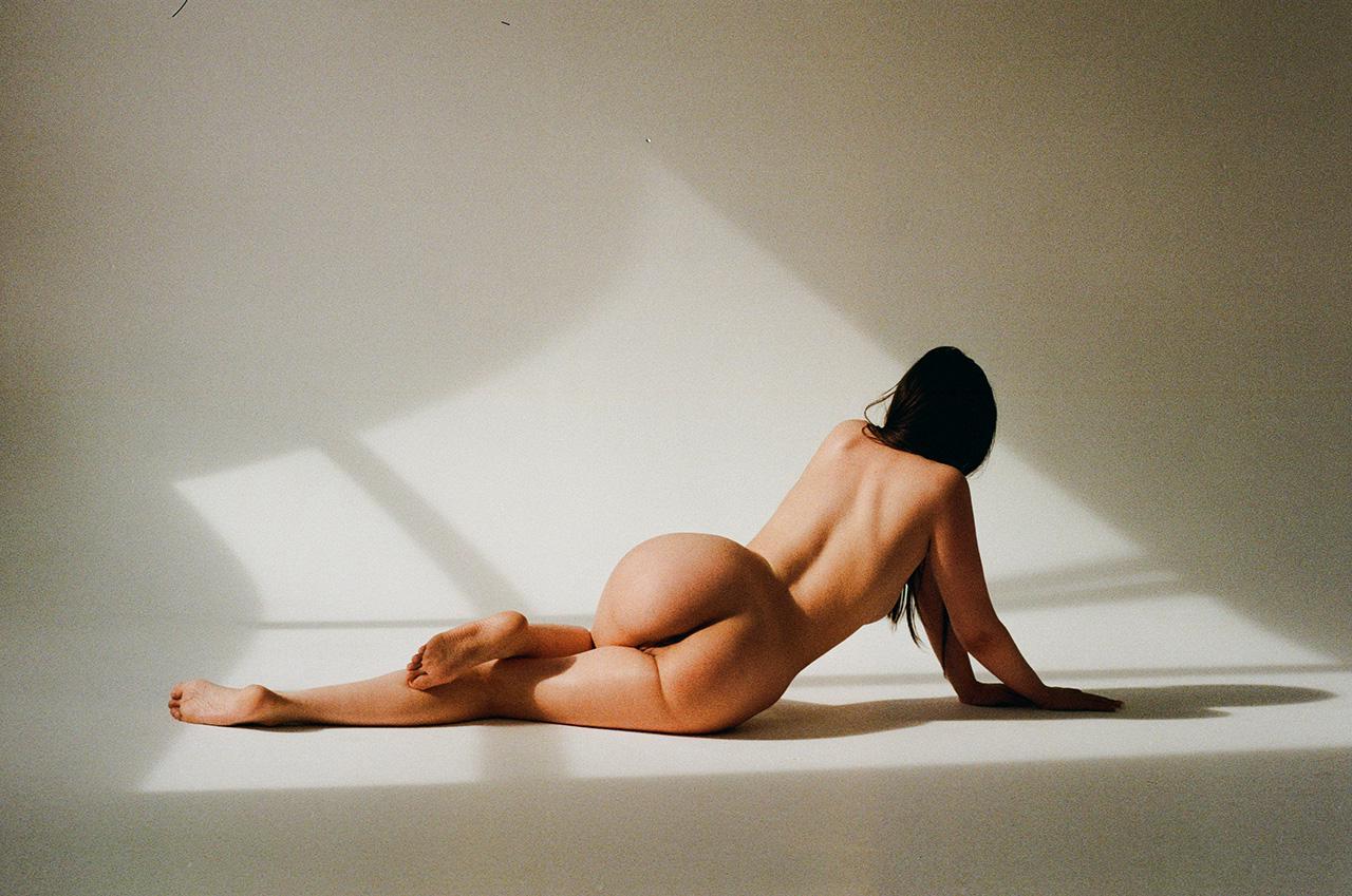 A woman is lying on her side on a light-colored surface with shadows cast across it.