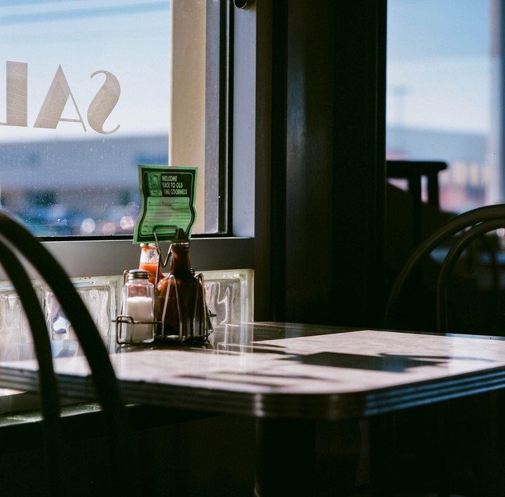 A table with condiments sits next to a window with a sign that reads "Welcome Back to Old Time Goodness."