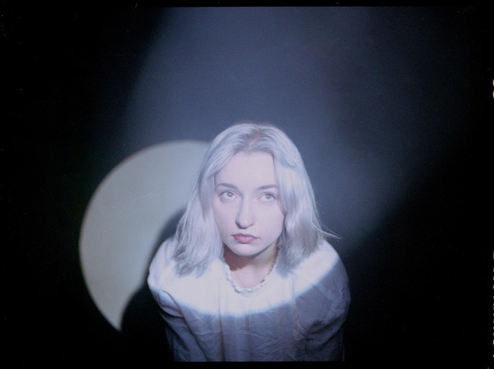 A woman with light hair looks up, illuminated by a spotlight against a dark background.