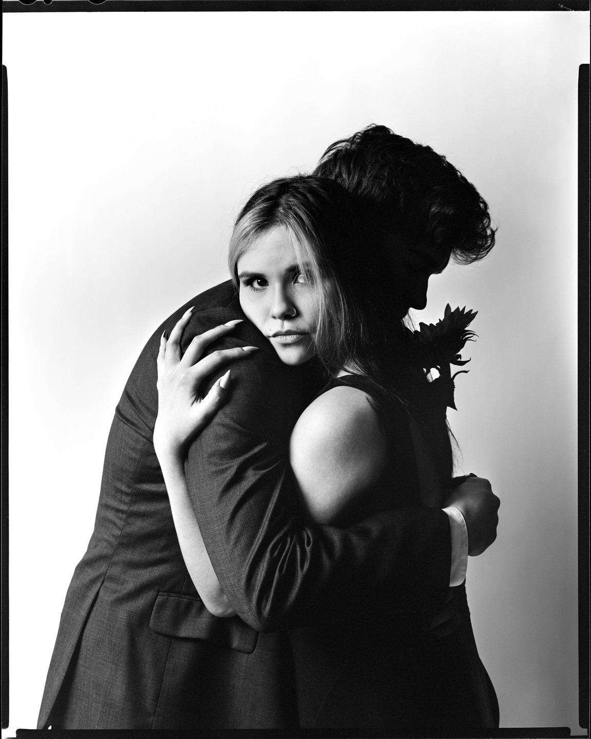 A woman embraces a man who holds a flower, with the man's face in shadow.