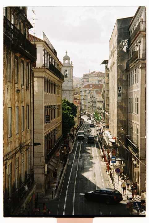 A street in Lisbon is filled with cars, people, and buildings under a bright sky.